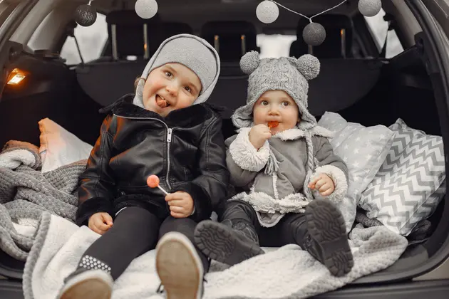 Divi mazi bērni ziemas drēbēs sēž uz auto bagažnieka