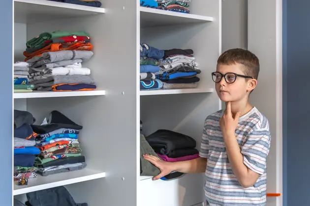 Puika ar brillēm stāv pie drē'bju skapja